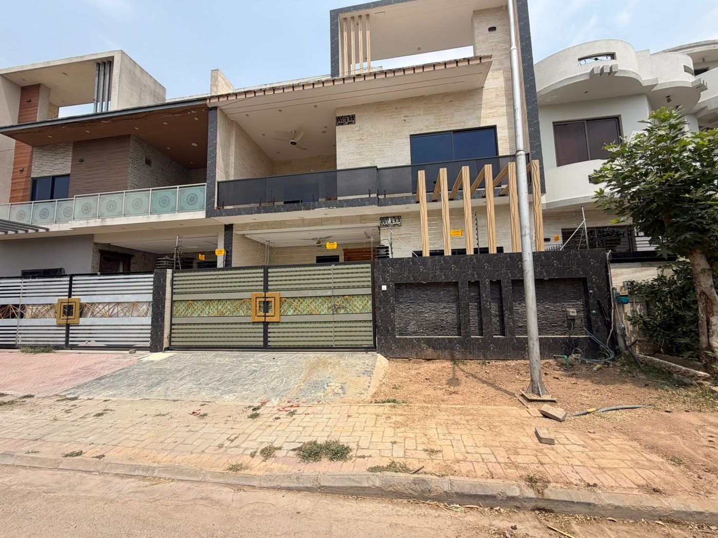 A two-storey family house built by G & S Builders — light stone cladding framed in black, a glass-railed first-floor terrace and timber-look fins at the entrance